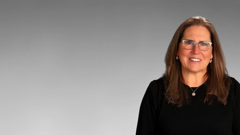 Professional woman, Merleta Mohr, in a black outfit with glasses smiling against a grey background.