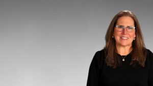 Professional woman, Merleta Mohr, in a black outfit with glasses smiling against a grey background.