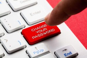 A finger is about to press a red key labeled "CHANGE YOUR PASSWORD" on a white keyboard with other standard keys, ensuring your password security is just one click away.