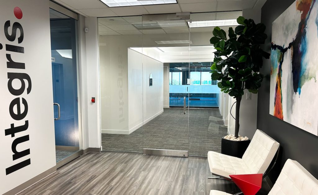 Modern office entry with glass doors, Integris logo on the left wall, white chairs, a plant, and abstract artwork on the right. For all your IT support needs in Dallas, our space combines functionality with style.