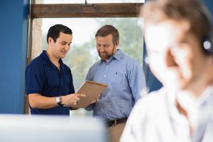 Two IT support men reviewing a document on a clipboard in an office setting.