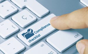 A finger is pressing a key labeled "Compliance checklist" on a white keyboard.