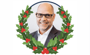 Man wearing glasses smiling inside a holly wreath illustration with red berries.