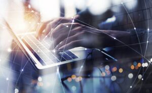 Close-up of hands typing on a laptop keyboard, overlaid with a network of connected lines and dots, symbolizing global digital connections.