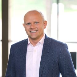 A smiling man in a blue patterned blazer and pink shirt.