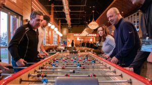 People playing a game of foosball inside a well-lit, spacious room with Holiday Lodge written on the wall in the background, enjoying a break from their work at an IT solution provider.
