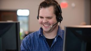 A smiling person with a headset in front of computer monitors in an office setting at an IT solution provider.