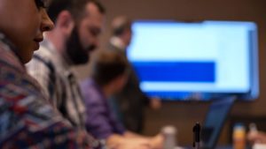 Professionals attending a presentation by an IT solution provider in a conference room with focus on a laptop screen.