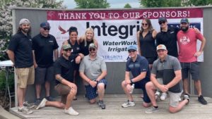 A group of people posing in front of a sponsorship banner that reads Thank you to our sponsors! with the names Integrity, WaterWorks Irrigation, and the leading IT solution provider.