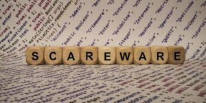 Wooden blocks spelling "SCAREWARE" placed on a background of scattered programming terms and codes.