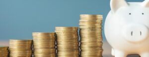 Stacks of gold coins in ascending height next to a white piggy bank against a blue background, illustrating smart savings as highlighted in recent press coverage.