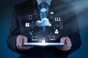 A person in a suit holds a tablet displaying holographic technology icons related to cloud computing and data security.