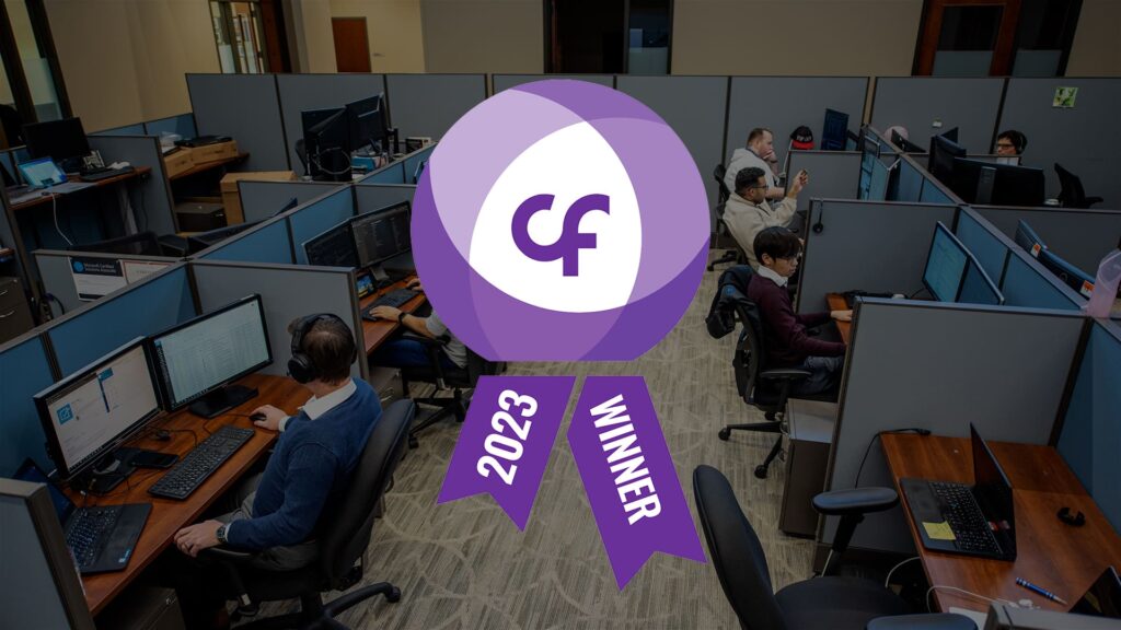 Office with several people working at computers in cubicles. A large "2023 Winner" badge with "cf" emblem is overlaid in the center.