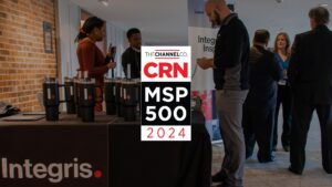 People are gathered at an event with a prominent sign that reads "The Channel Co. CRN MSP 500 2024." Booth displays feature the logo "Integris," and attendees are engaging in conversations near the booths. The atmosphere is professional and business-oriented.