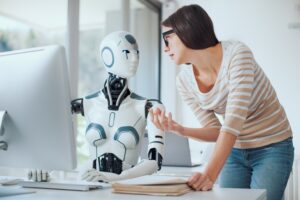 A woman in a striped shirt and glasses converses with a humanoid robot sitting at a computer desk, discussing the latest updates for Copilot for Microsoft Teams. The background features a modern office setting with large windows. The robot has a white body with black accents and blue lights for eyes.