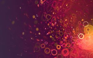 Abstract digital image with glowing hexagons and circles in pink, orange, and yellow tones scattered over a dark purple background.