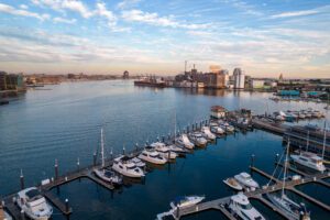 A marina with numerous docked boats in the foreground, a calm harbor, and city buildings—home to managed IT in Owings Mills, MD—under a partly cloudy sky in the background.
