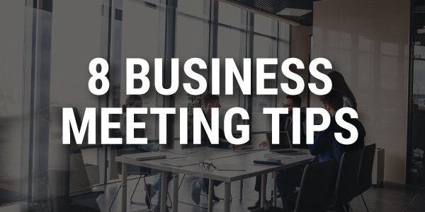 A group of people sitting around a conference table in a modern office setting. The text overlay reads, 8 Business Meeting Tips.
