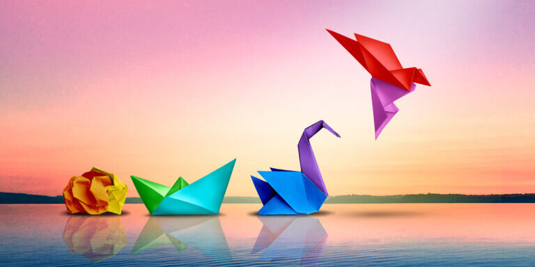 Four colorful origami shapes—a crumpled ball, boat, swan, and flying bird—are arranged on calm water against a pastel sunset sky.