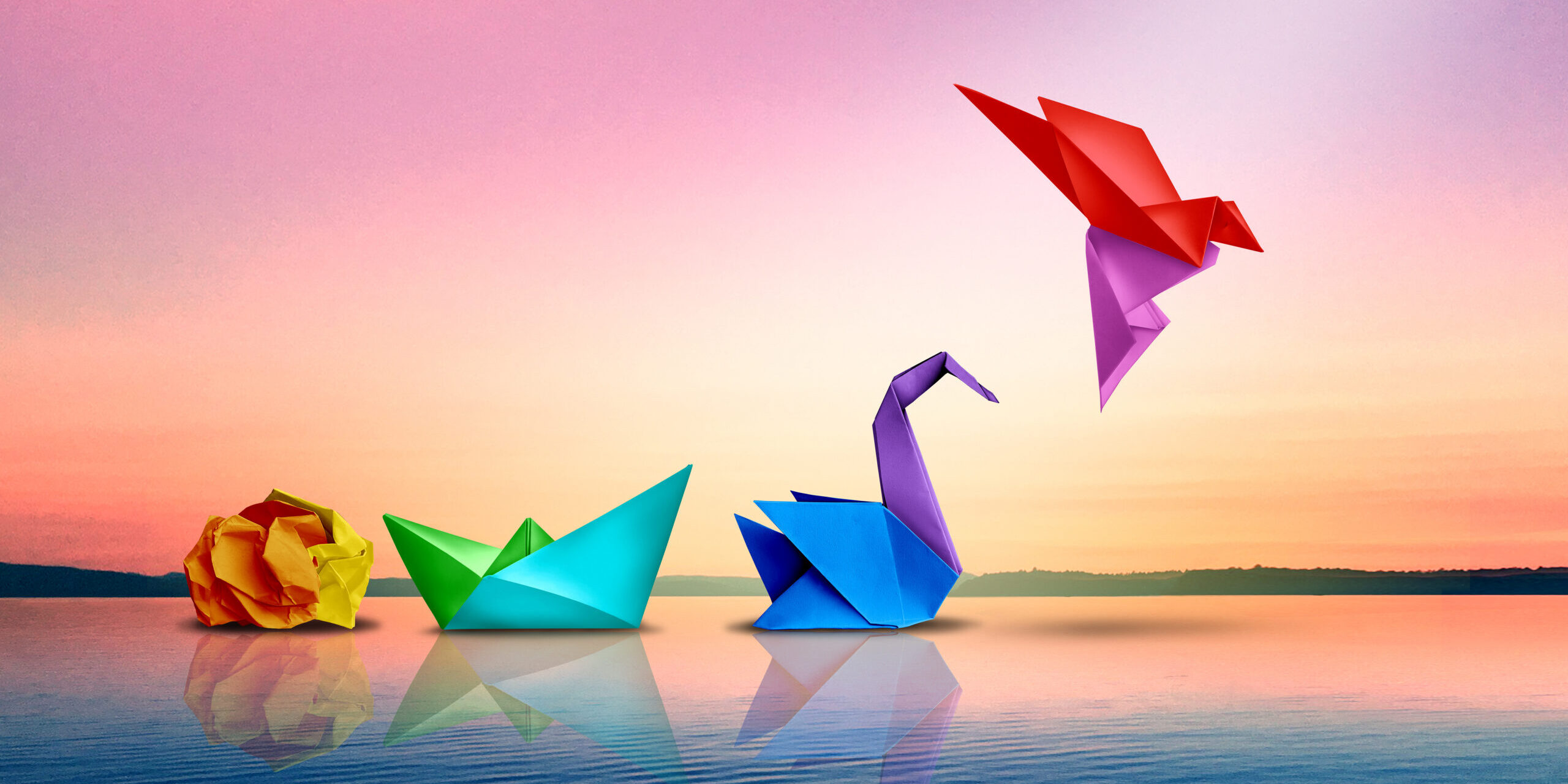 Four colorful origami shapes—a crumpled ball, boat, swan, and flying bird—are arranged on calm water against a pastel sunset sky.