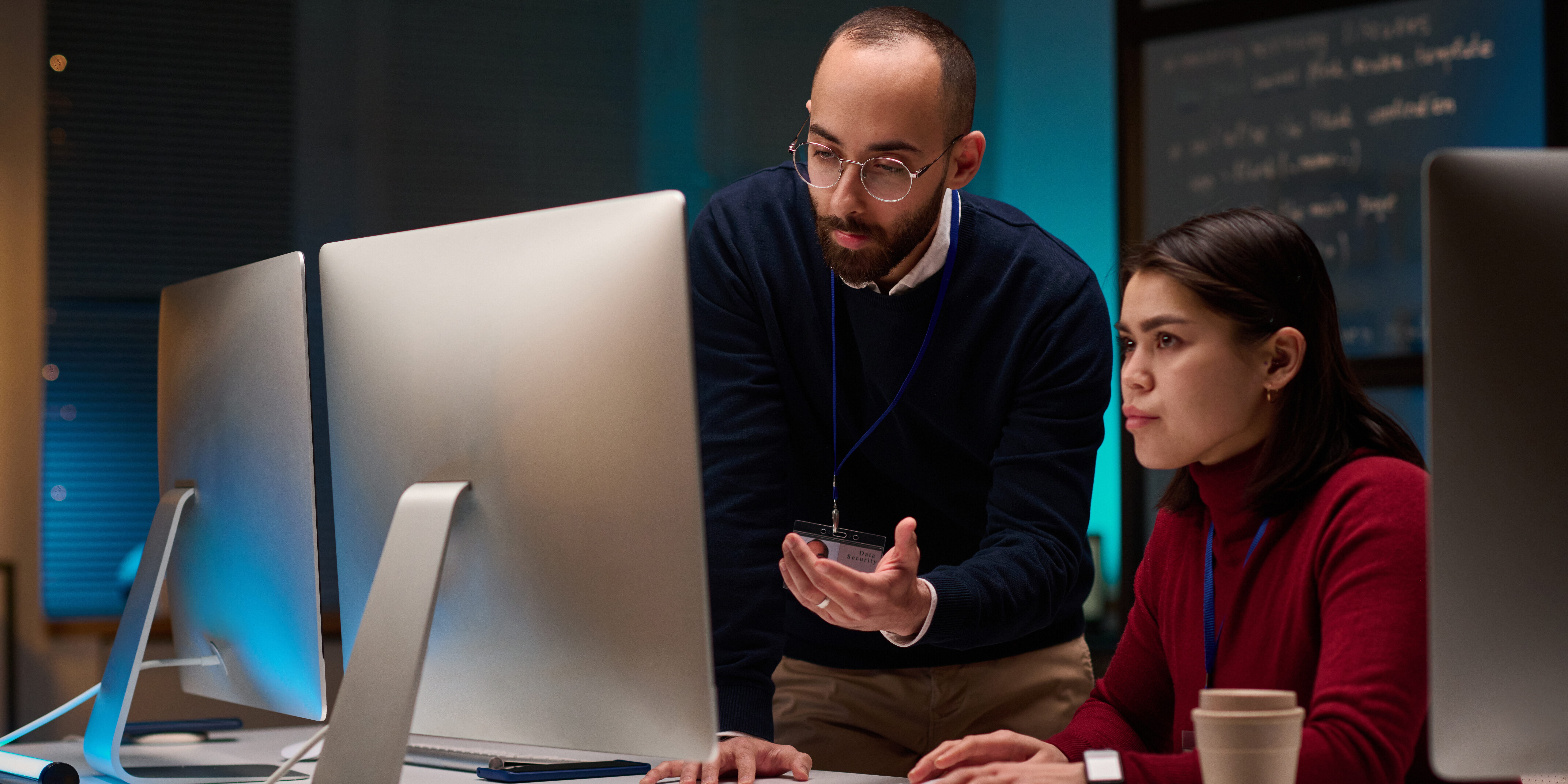 Minimal portrait of two people using computers while working in cybersecurity department with blue lights