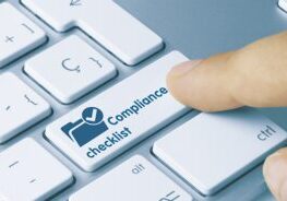 A finger is pressing a key labeled "Compliance checklist" on a white keyboard.
