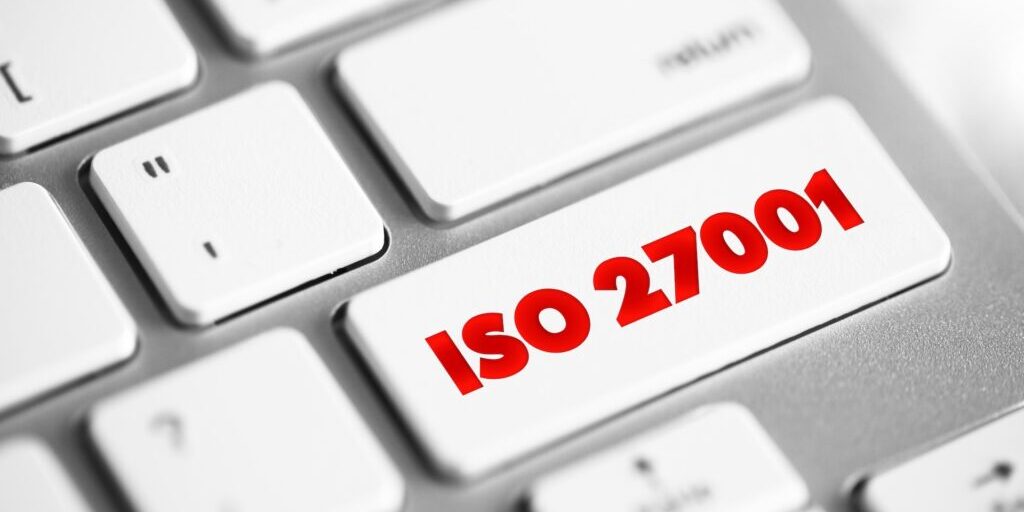 Close-up of a computer keyboard with a white key labeled "ISO 27001" in red text, emphasizing the importance of this information security standard. The surrounding keys are visible, showcasing a typical QWERTY layout.