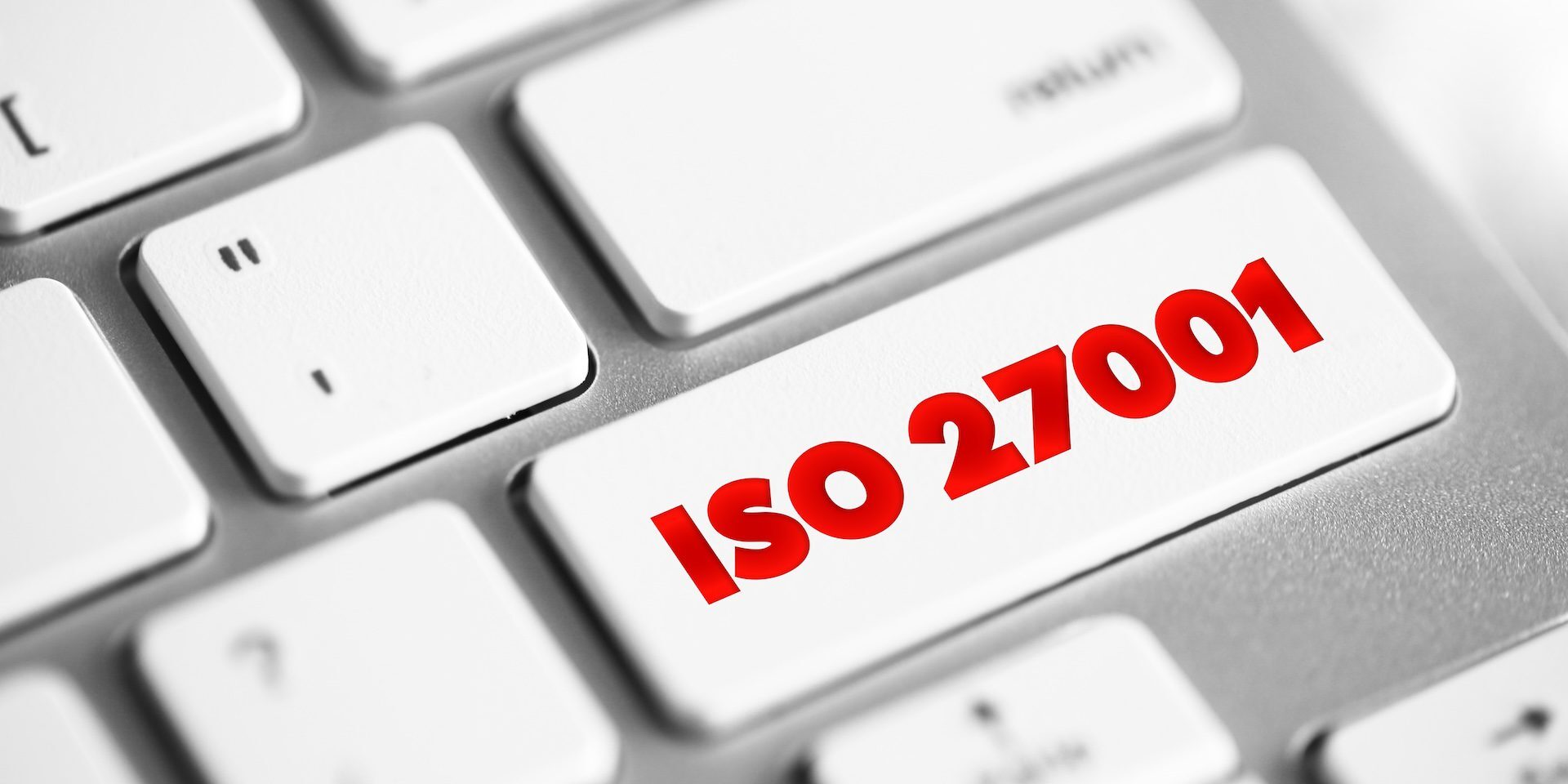 Close-up of a computer keyboard with a white key labeled "ISO 27001" in red text, emphasizing the importance of this information security standard. The surrounding keys are visible, showcasing a typical QWERTY layout.