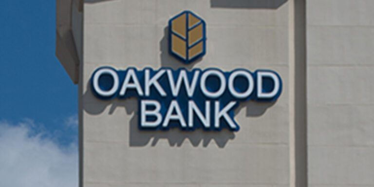 The exterior wall of a building displays the Oakwood Bank sign in blue and gold, featuring its geometric logo.