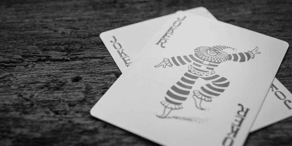 Black and white image of two overlapping Joker playing cards on a wooden surface.