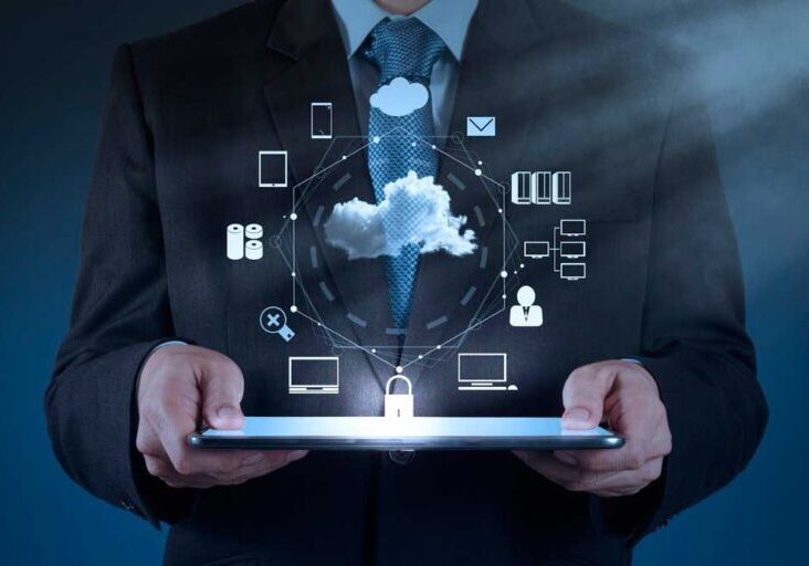 A person in a suit holds a tablet displaying holographic technology icons related to cloud computing and data security.