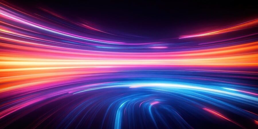 Abstract image of bright, colorful light trails in shades of orange, pink, and blue curving across a dark background, giving a sense of motion and energy.