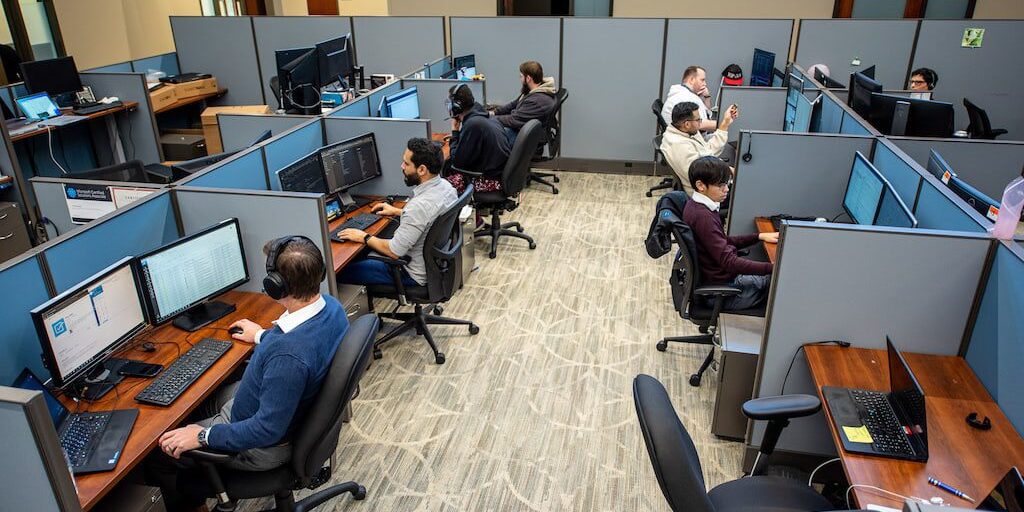 Office workers busy at their desks in a modern cubicle workspace.