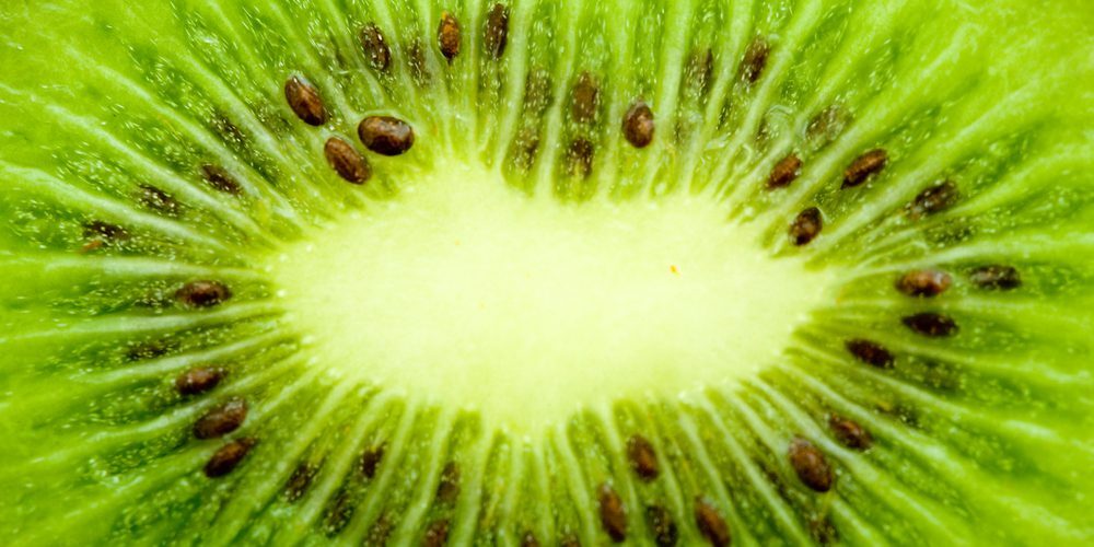 Close-up of a sliced kiwi fruit showing its green flesh, black seeds, and radial pattern extending from the center.