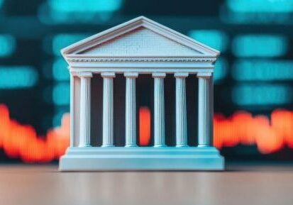 A model of a classical bank building with columns is in front of a blurred background showing red and blue financial stock market data.
