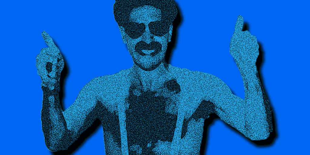 A man wearing sunglasses and minimal clothing gestures with both hands pointing upwards against a blue background.