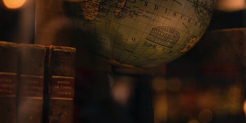 A vintage globe sits on a map beside three old books, illuminated by soft, warm lighting.