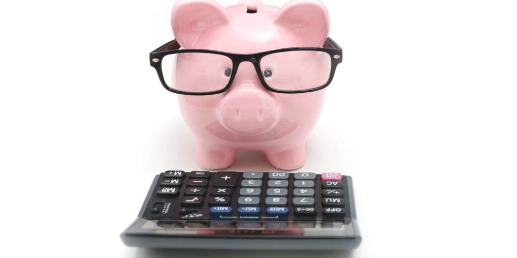 A pink piggy bank sporting glasses stands behind a calculator, symbolizing financial planning and savings.