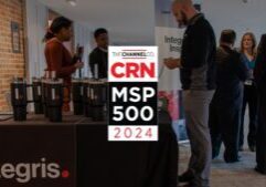 People are gathered at an event with a prominent sign that reads "The Channel Co. CRN MSP 500 2024." Booth displays feature the logo "Integris," and attendees are engaging in conversations near the booths. The atmosphere is professional and business-oriented.