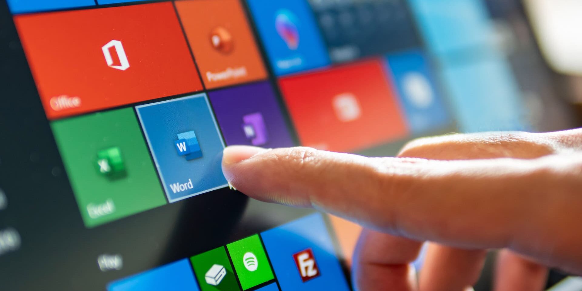 A finger taps the Word icon on a Windows touch screen, surrounded by various other application icons like Excel, PowerPoint, and Mail. Spend Smarter: A Microsoft 365 Licensing Guide can help you navigate these applications efficiently.