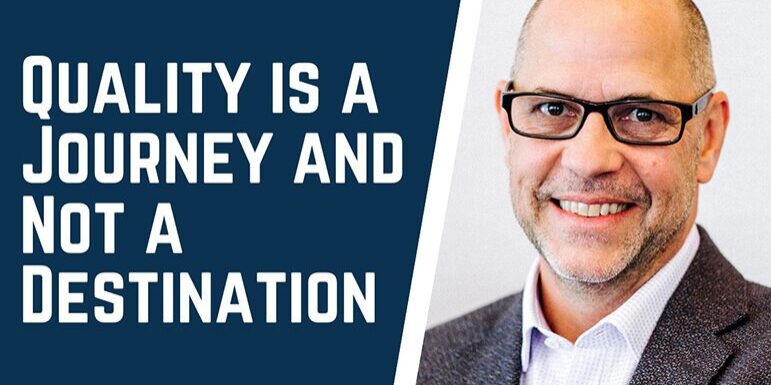 Man smiling with glasses in a suit on the right, text on the left reads QUALITY IS A JOURNEY AND NOT A DESTINATION.