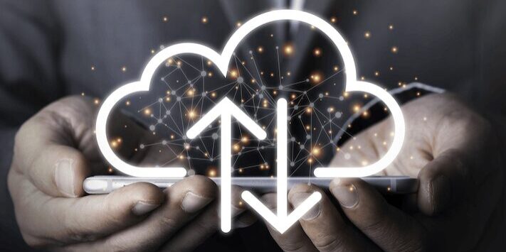 Hands holding a smartphone display a digital cloud hologram with arrows indicating upload and download.