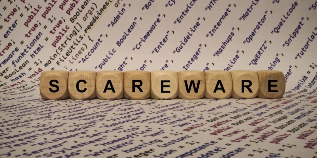 Wooden blocks spelling "SCAREWARE" placed on a background of scattered programming terms and codes.