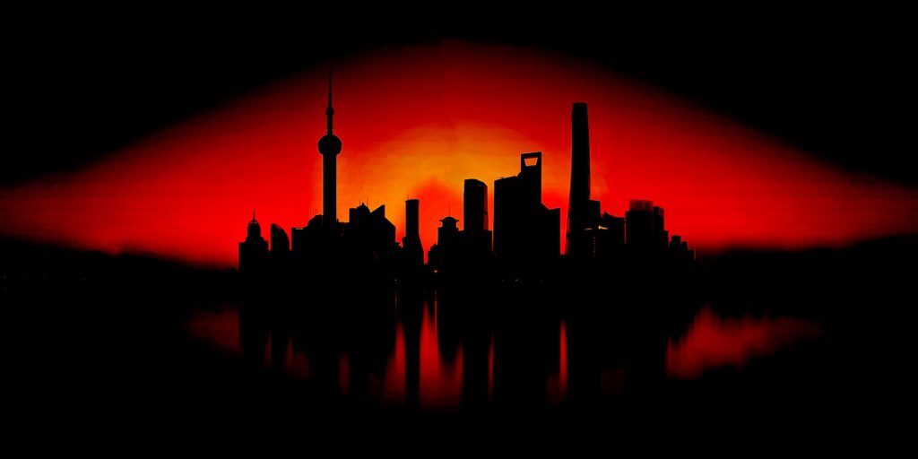 Silhouette of a city skyline with various skyscrapers and towers set against a vivid red and black sunset background, reflecting on a body of water, symbolizing the vigilance and protection akin to cybersecurity measures guarding our digital world.
