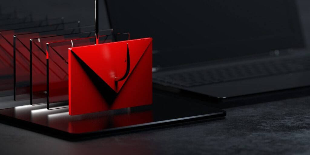 A deceptive red email icon is being hooked, indicating a phishing attack. The scene includes a laptop and black reflective surfaces, highlighting the seriousness of these digital threats.