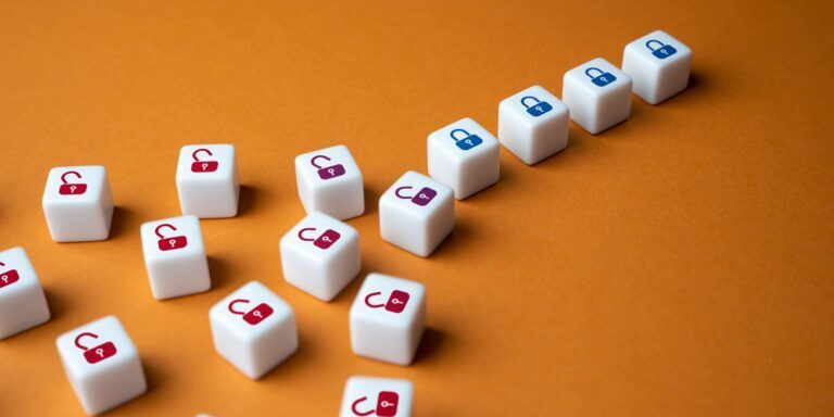 Various white cubes with red, maroon, and blue padlock icons, both unlocked and locked, are arranged diagonally against an orange background. The cubes with blue padlocks—reminiscent of an FFIEC Audit setup—are grouped together in a straight row, with the rest scattered.