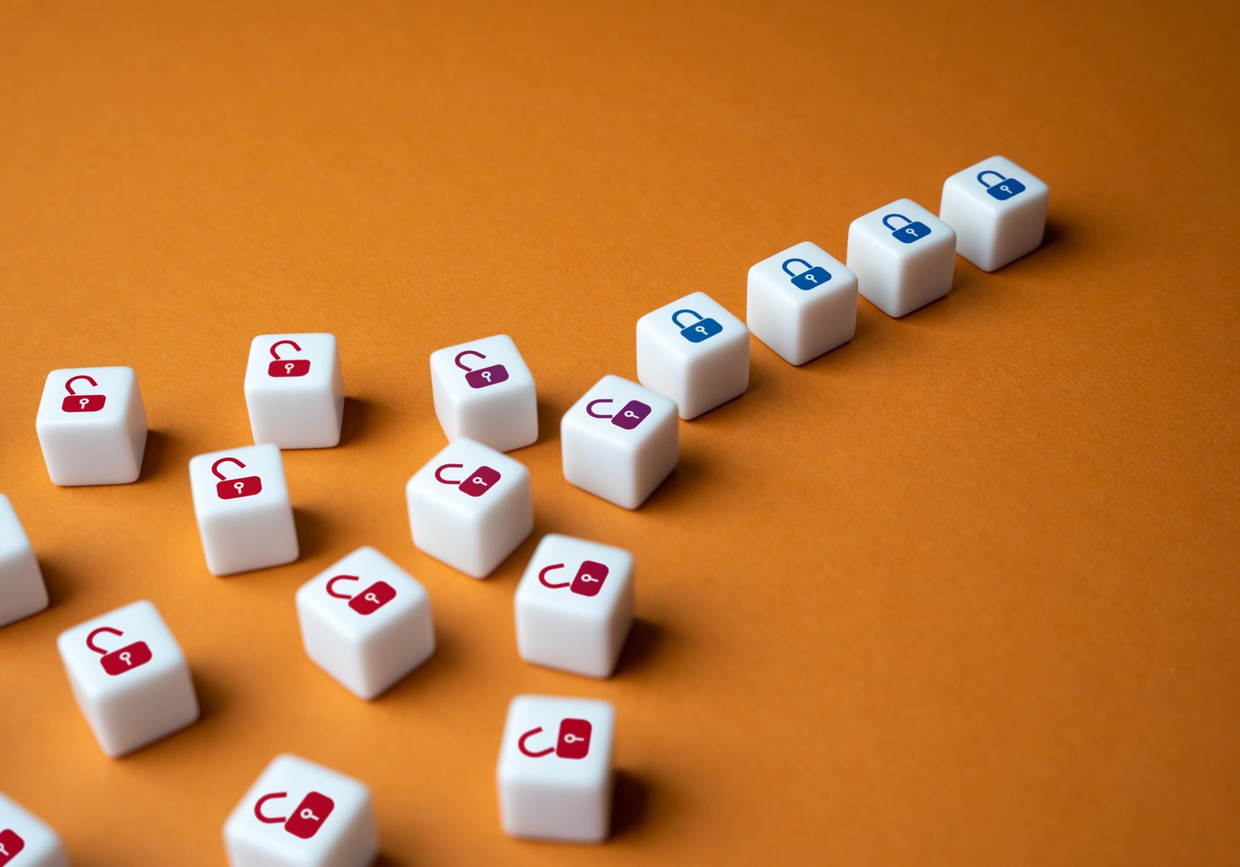 Various white cubes with red, maroon, and blue padlock icons, both unlocked and locked, are arranged diagonally against an orange background. The cubes with blue padlocks—reminiscent of an FFIEC Audit setup—are grouped together in a straight row, with the rest scattered.