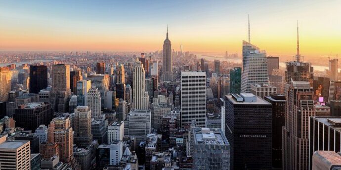 Aerial view of a sprawling New York City with numerous skyscrapers at sunset, including a prominent, tall building in the center. The scene reflects the dynamic environment that benefits from Managed IT Services New York City is known for.