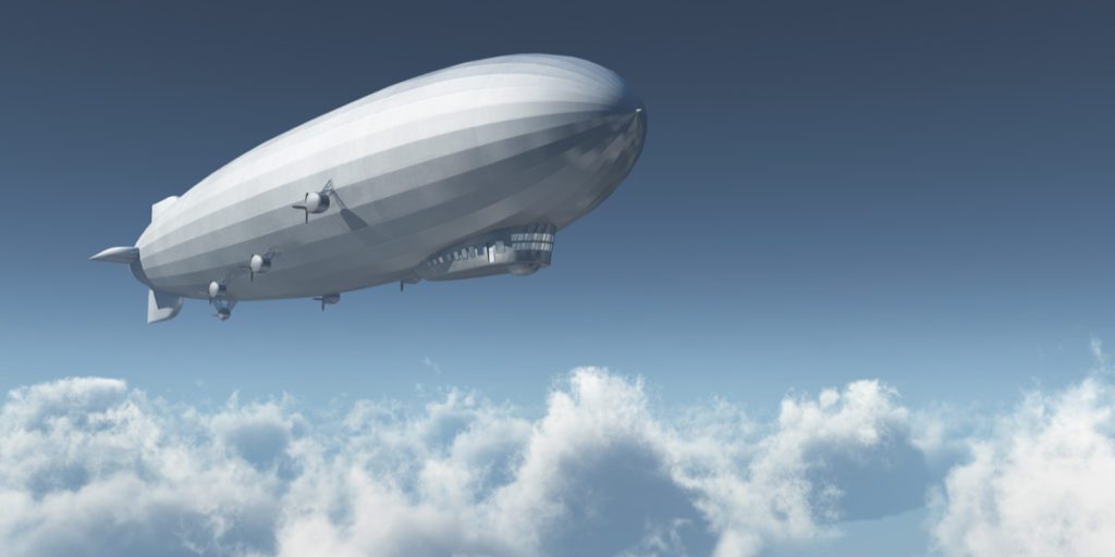A large airship floats above the clouds in a clear sky.