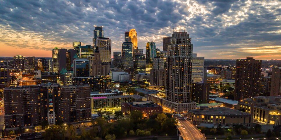 Aerial view of Minneapolis city skyline at dusk with illuminated buildings under a cloud-filled sky, highlighting the tech hub's thriving IT support network.